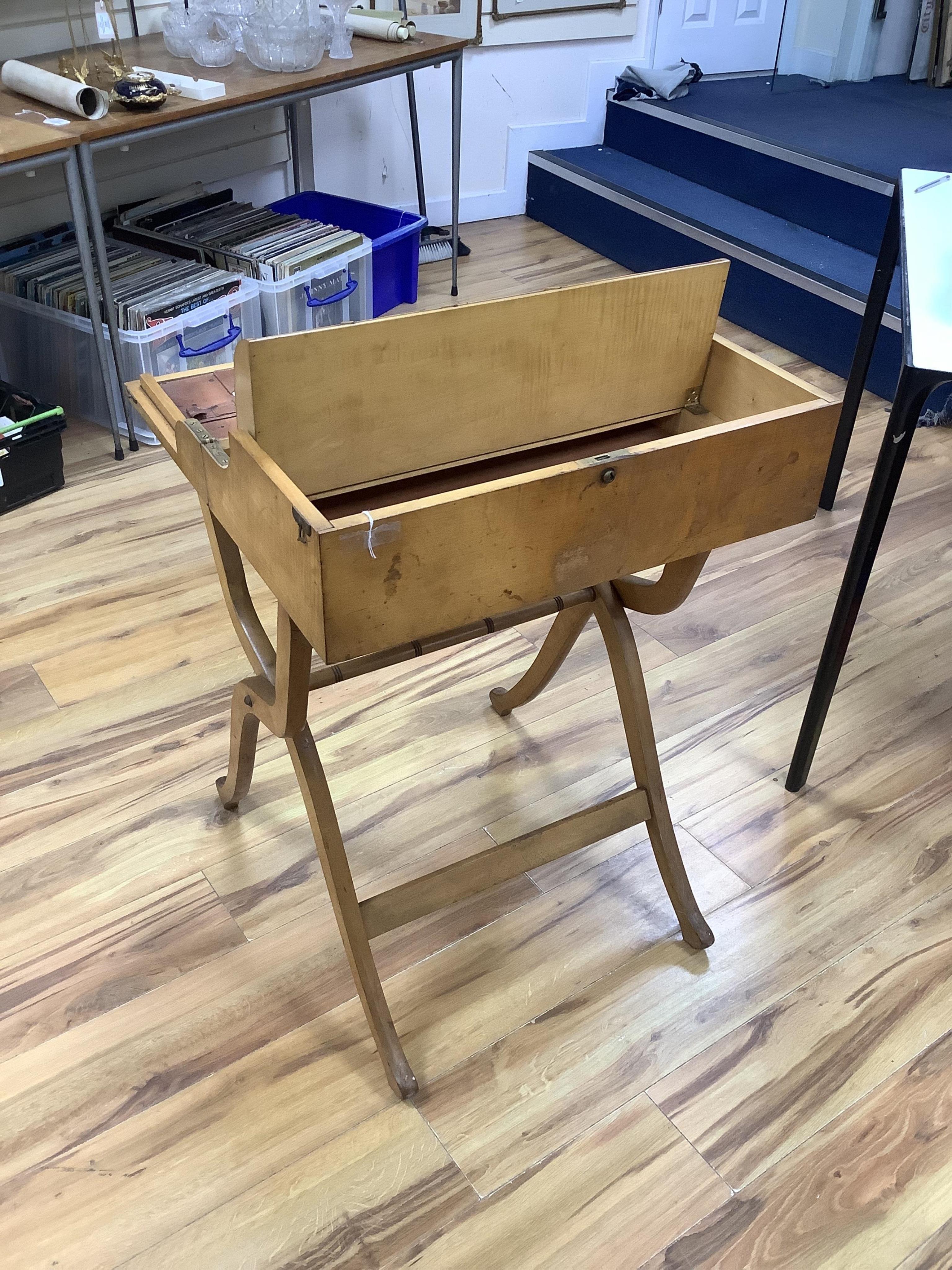 A late 19th century sycamore military folding campaign desk, raised on a trestle stand with X shaped supports, desk section with leather writing surface and folding letter rack, 93cm high, 56cm wide when folded. Conditio